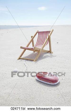 Stock Image - sunlounger and computer mouse on sandy beach. Fotosearch