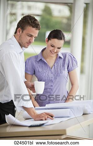 Stock Image - two business people at table looking at blueprint. Fotosearch