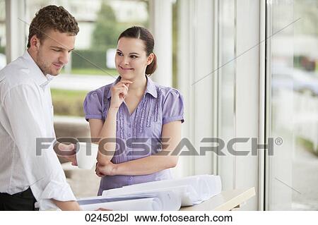 Stock Image - two business people at table looking at blueprint. Fotosearch