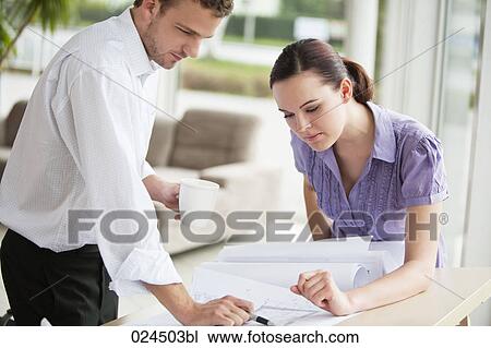 Stock Image - two business people at table looking at blueprint. Fotosearch