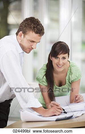 Stock Image - two business people working on blueprint together. Fotosearch