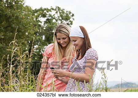 Stock Image - two young woman reading text message on mobile phone. Fotosearch
