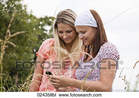 Stock Image - two young woman reading text message on mobile phone. Fotosearch