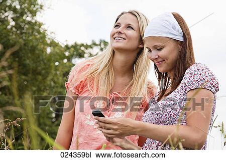 Stock Image - two young woman reading text message on mobile phone. Fotosearch
