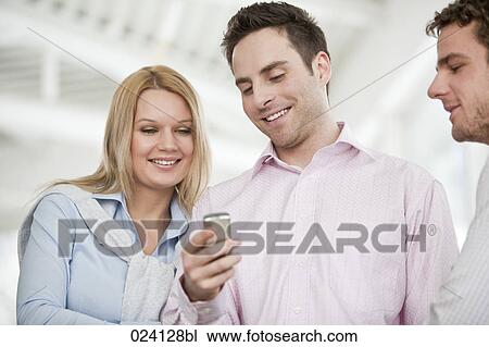 Stock Image - young businessman showing text message on mobile phone to colleague. Fotosearch