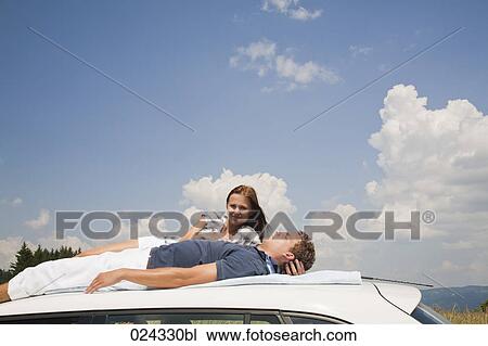 Stock Image - young couple lying on roof of car. Fotosearch