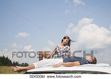 Stock Image - young couple lying on roof of car. Fotosearch