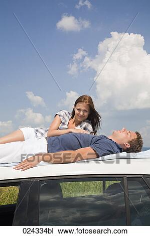 Stock Image - young couple lying on roof of car. Fotosearch