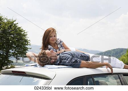 Stock Image - young couple lying on roof of car. Fotosearch