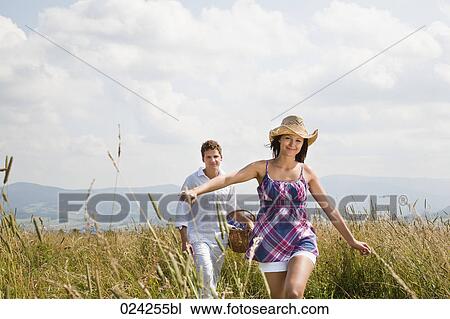 Stock Image - young couple with picnic basket walking through field. Fotosearch