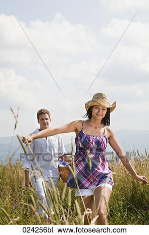 Stock Image - young couple with picnic basket walking through field. Fotosearch