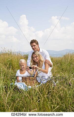 Stock Image - young family taking self-portrait with digital camera in field. Fotosearch
