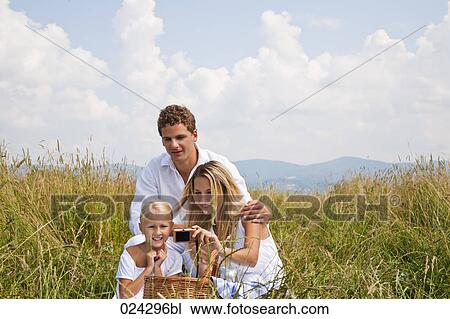 Stock Image - young family taking self-portrait with digital camera in field. Fotosearch