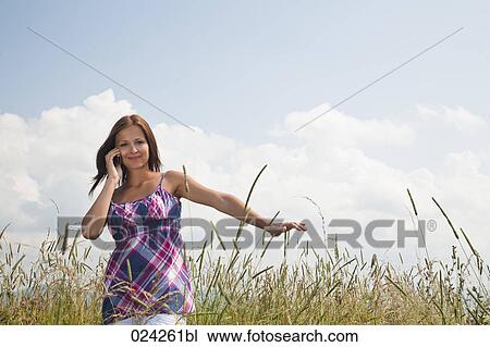 Stock Image - young woman in field talking on mobile phone. Fotosearch