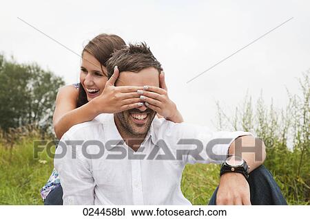 Stock Image - young woman playing peekaboo with boyfriend. Fotosearch