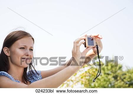 Stock Image - young woman taking picture of herself with digital camera. Fotosearch