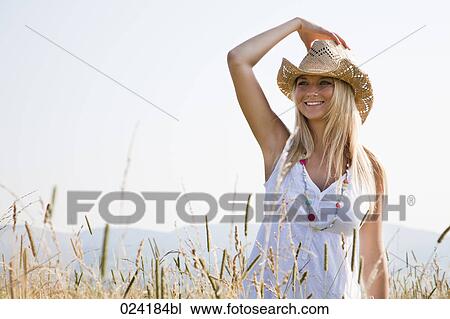 Stock Image - young woman with hat standing in field. Fotosearch