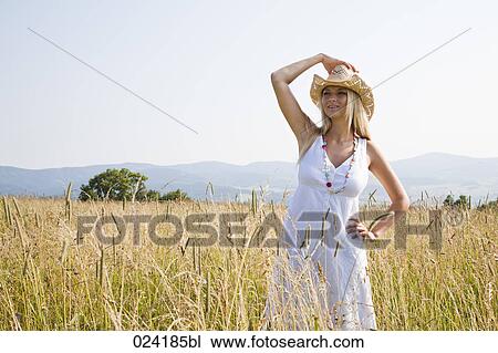 Stock Image - young woman with hat standing in field. Fotosearch