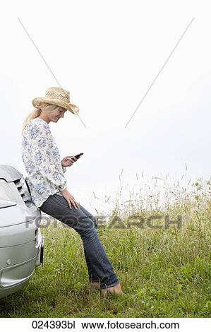 Stock Image - young woman with mobile phone leaning against car. Fotosearch