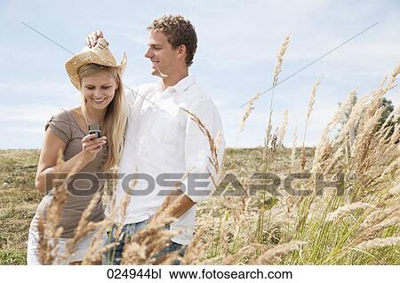 Stock Image - portrait of young couple in field woman lloking at display of mobile phone. Fotosearch