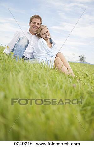 Stock Image - portrait of young couple sitting in grass. Fotosearch