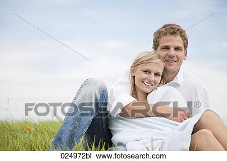 Stock Image - portrait of young couple sitting in grass. Fotosearch