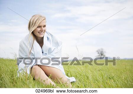 Stock Image - portrait of young woman covered with blanket sitting in grass. Fotosearch