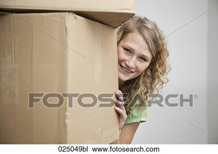 Stock Image - portrait of young woman hiding behind cardboard boxes. Fotosearch