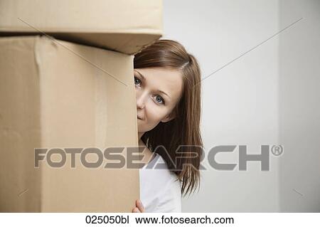 Stock Image - portrait of young woman hiding behind cardboard boxes. Fotosearch