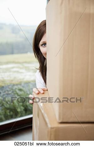 Stock Image - portrait of young woman hiding behind cardboard boxes. Fotosearch