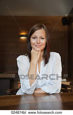 Stock Image - portrait of young woman sitting at restaurant table. Fotosearch