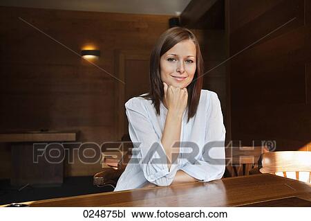 Stock Image - portrait of young woman sitting at restaurant table. Fotosearch
