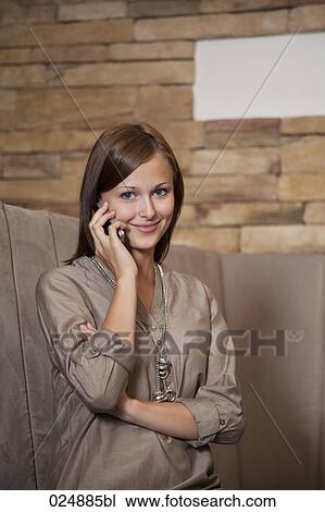 Stock Image - portrait of young woman talking on mobile phone at restaurant. Fotosearch