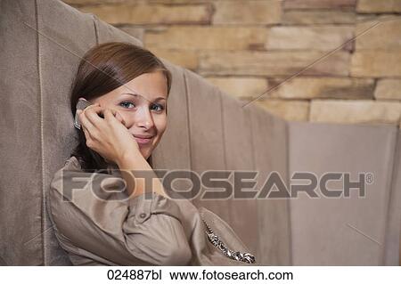 Stock Image - portrait of young woman talking on mobile phone at restaurant. Fotosearch