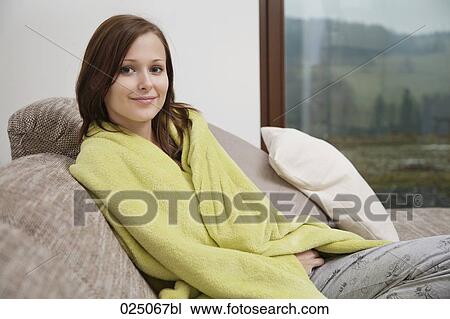 Stock Image - portrait of young woman wrapped in blanket on sofa. Fotosearch