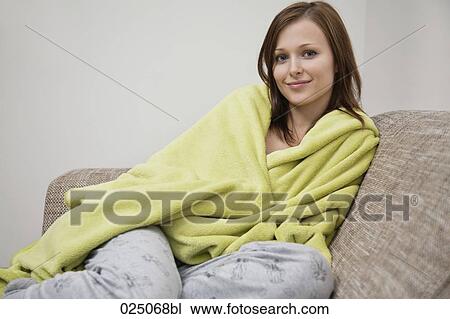 Stock Image - portrait of young woman wrapped in blanket on sofa. Fotosearch