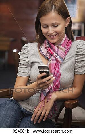 Stock Image - smiling young woman looking at display of her mobile phone. Fotosearch
