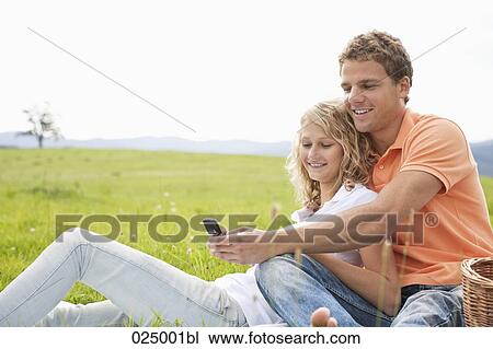 young couple having picnic looking at display of mobile phone View Large Photo Image Stock Image - young couple having picnic looking at display of mobile phone. Fotosearch