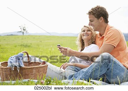 Stock Image - young couple having picnic looking at display of mobile phone. Fotosearch