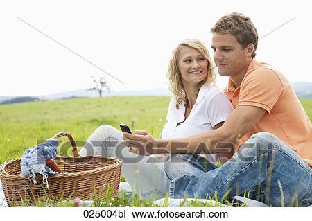 young couple having picnic looking at display of mobile phone View Large Photo Image Stock Image - young couple having picnic looking at display of mobile phone. Fotosearch