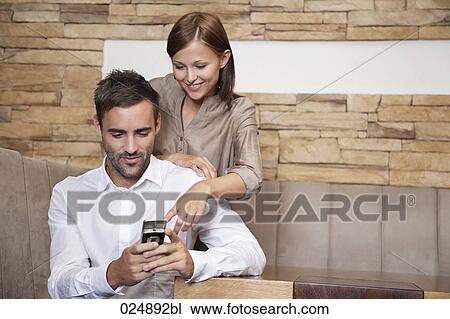 Stock Image - young couple reading message on moile phone at restaurant. Fotosearch