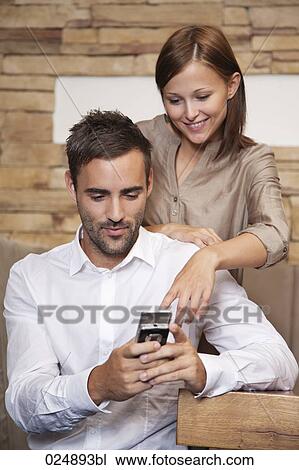 Stock Image - young couple reading message on moile phone at restaurant. Fotosearch