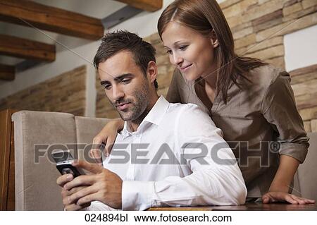 Stock Image - young couple reading message on moile phone at restaurant. Fotosearch