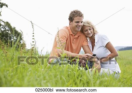 Stock Image - young couple sitting in meeting looking at display of mobile phone. Fotosearch