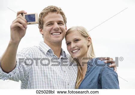 Stock Image - young couple taking picture of themselves with digital camera. Fotosearch