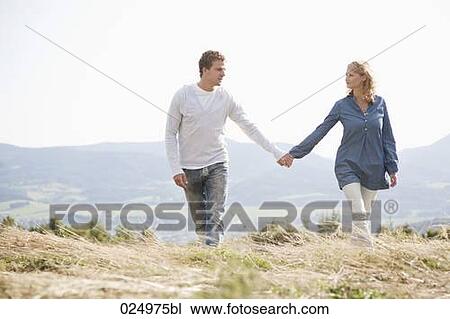 Stock Image - young couple walking through field hand in hand. Fotosearch