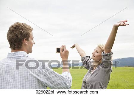 Stock Image - young man taking picture of young woman with digital camera. Fotosearch