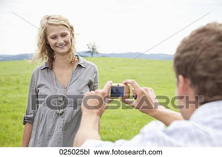 Stock Image - young man taking picture of young woman with digital camera. Fotosearch