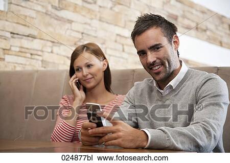 Stock Image - young woman and man with mobile phones at restaurant. Fotosearch