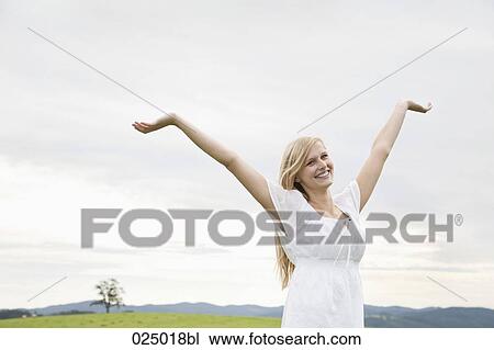 young woman on meadow raising her arms in the air View Large Photo Image Stock Image - young woman on meadow raising her arms in the air. Fotosearch